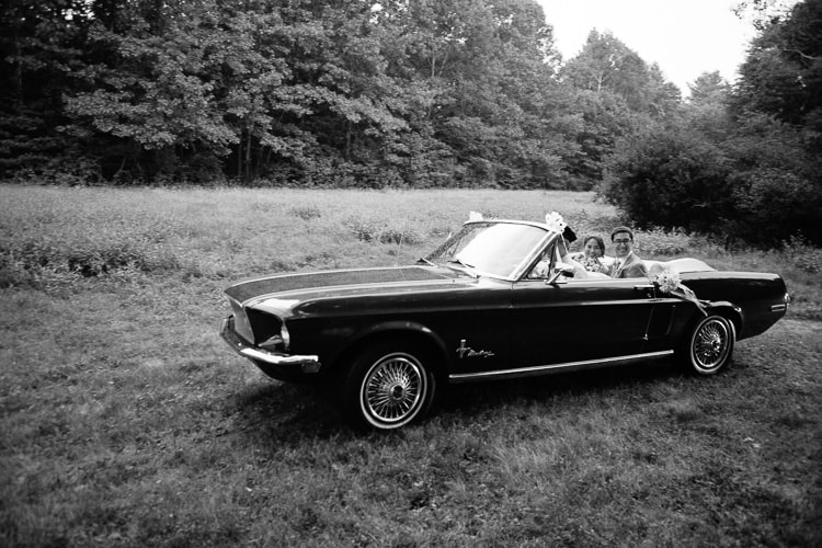 bride and groom exit the ceremony in a convertible in the rain