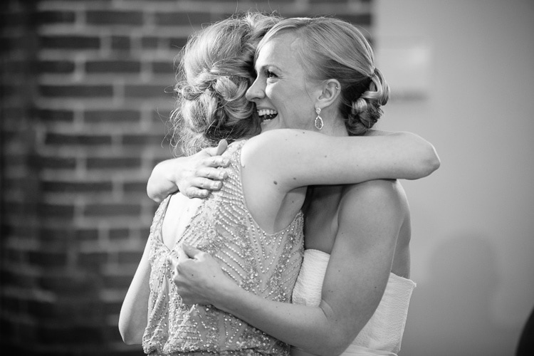 bride embraces sister after toast at her Charles River Museum wedding reception