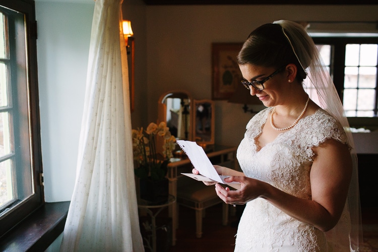 bride stands in window light reading groom's letter, Willowdale Estate, image by Kelly Benvenuto