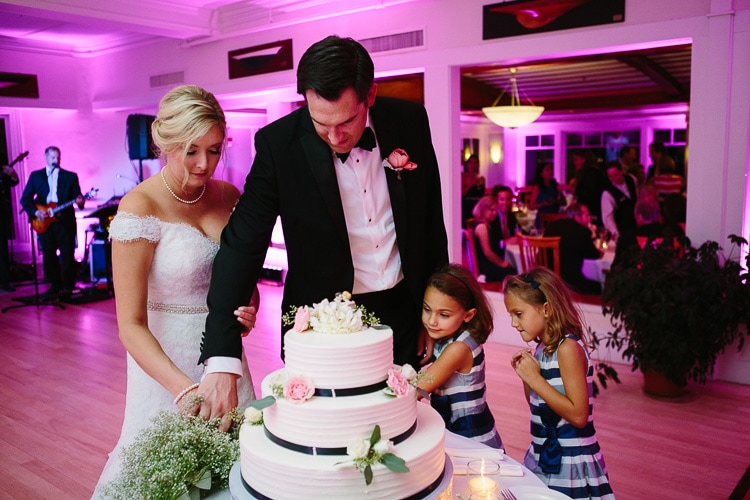 bride and groom cut cake, with help from flower girls