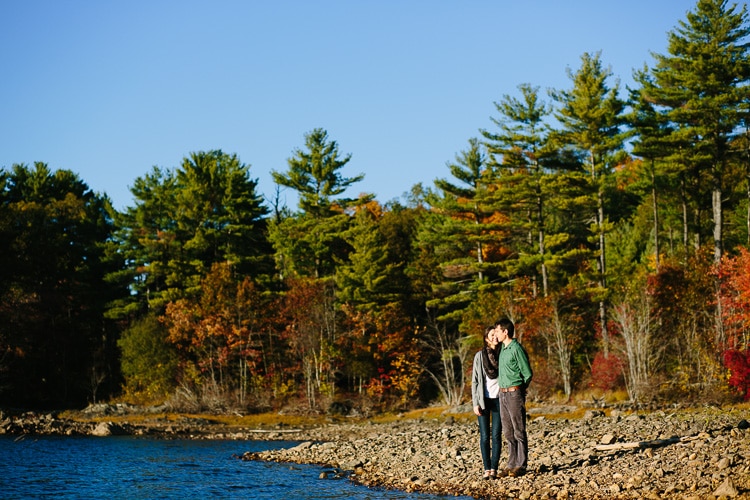 New England, fall engagement photo, with water and pine trees. Image by Kelly Benvenuto.
