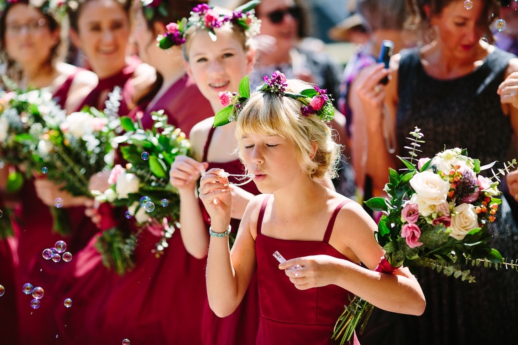 Junior bridesmaid blows bubbles outside the church following the wedding ceremony. Colorful, vibrant wedding photography by Kelly Benvenuto.