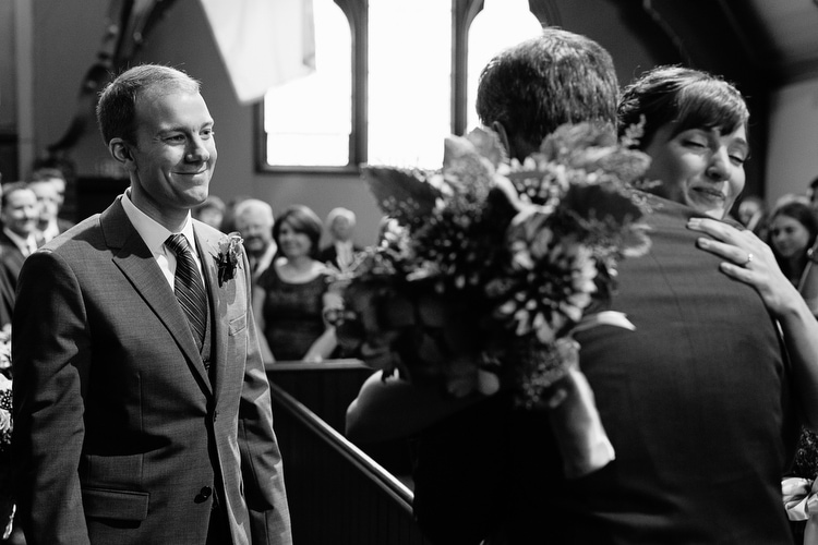 Bride hugs her dad at the top of the aisle while groom looks on. Honest, emotional, documentary wedding photography in Boston and New England. Image by Kelly Benvenuto.