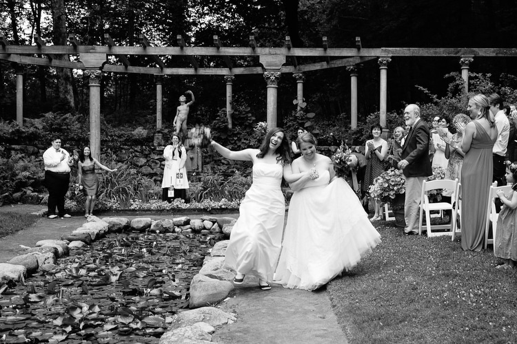 Brides dance up the aisle at the end of their wedding ceremony in the garden of the Codman Estate in Lincoln, MA. Candid wedding photography near Boston by Kelly Benvenuto.