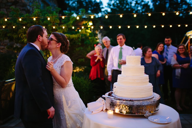 Bride and groom share a kiss after cutting the cake at the Willowdale Estate. Vibrant, authentic wedding photography by Kelly Benvenuto.