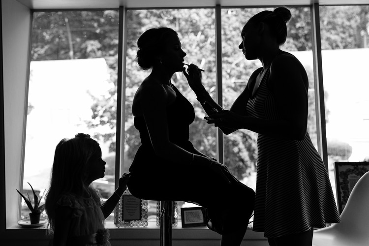 Silhouette of flower girl, bridesmaid and makeup artist, getting ready before a wedding. Artistic wedding photojournalism by Boston wedding photographer Kelly Benvenuto.