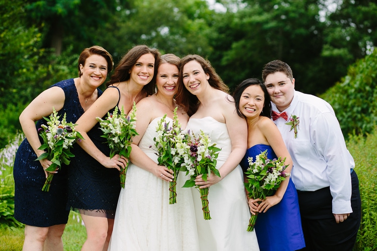 Relaxed wedding party portrait with two brides on the grounds of the Codman Estate in Lincoln, MA. Colorful, natural wedding photography by Kelly Benvenuto.