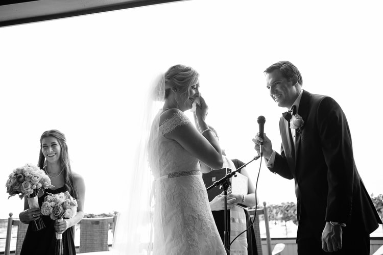 An emotional moment as groom recites vows, bride cries, and bridesmaid smiles during a ceremony on the porch of the Corinthian Yacht Club in Marblehead, MA. Black and white, documentary wedding photography by Kelly Benvenuto, serving Boston and New England.