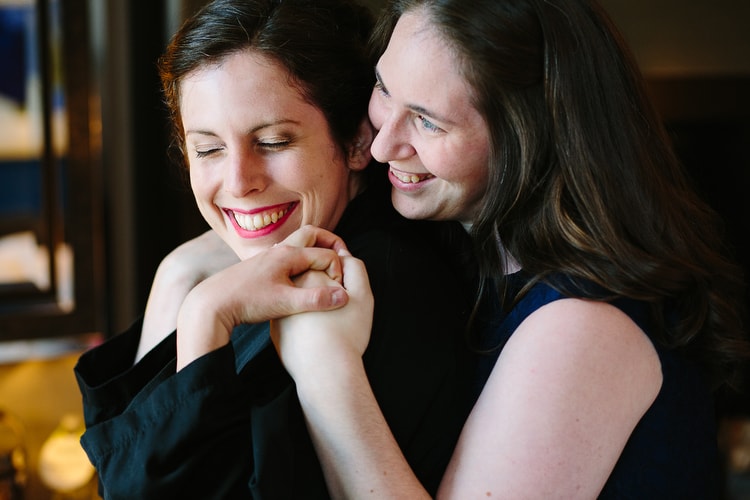 Bride and bridesmaid share a smile and a squeeze while getting ready. Cambridge, Massachusetts documentary wedding by Kelly Benvenuto.