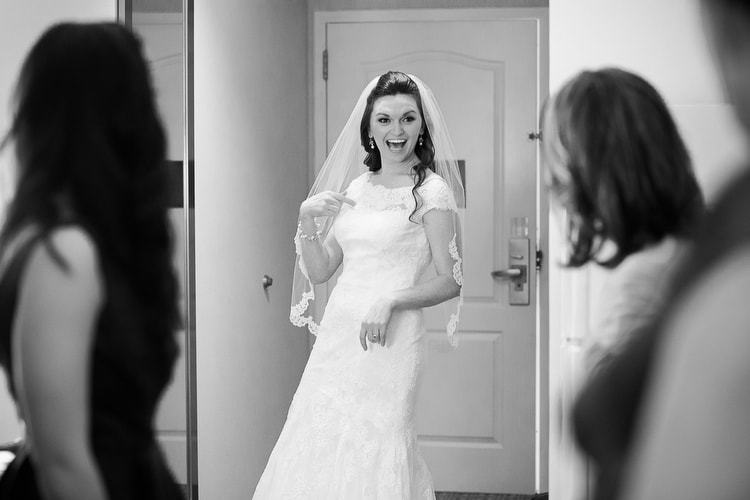 Bride sees herself for first time in all her wedding attire and exclaims to mother and bridesmaids. Documentary New Hampshire wedding photography by Kelly Benvenuto.