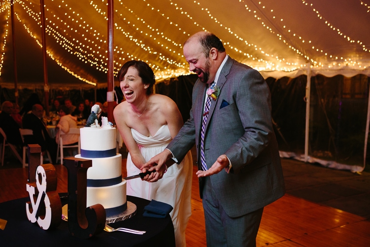 Bride and groom laugh while cutting the cake. Candid wedding photography in Boston and New England by Kelly Benvenuto.