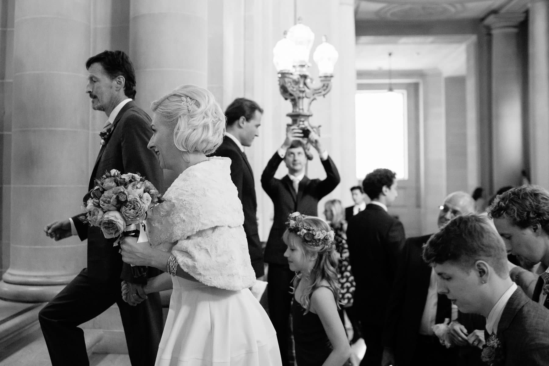 bride, groom and guests climb stairs to the rotunda at San Francisco City Hall for their wedding