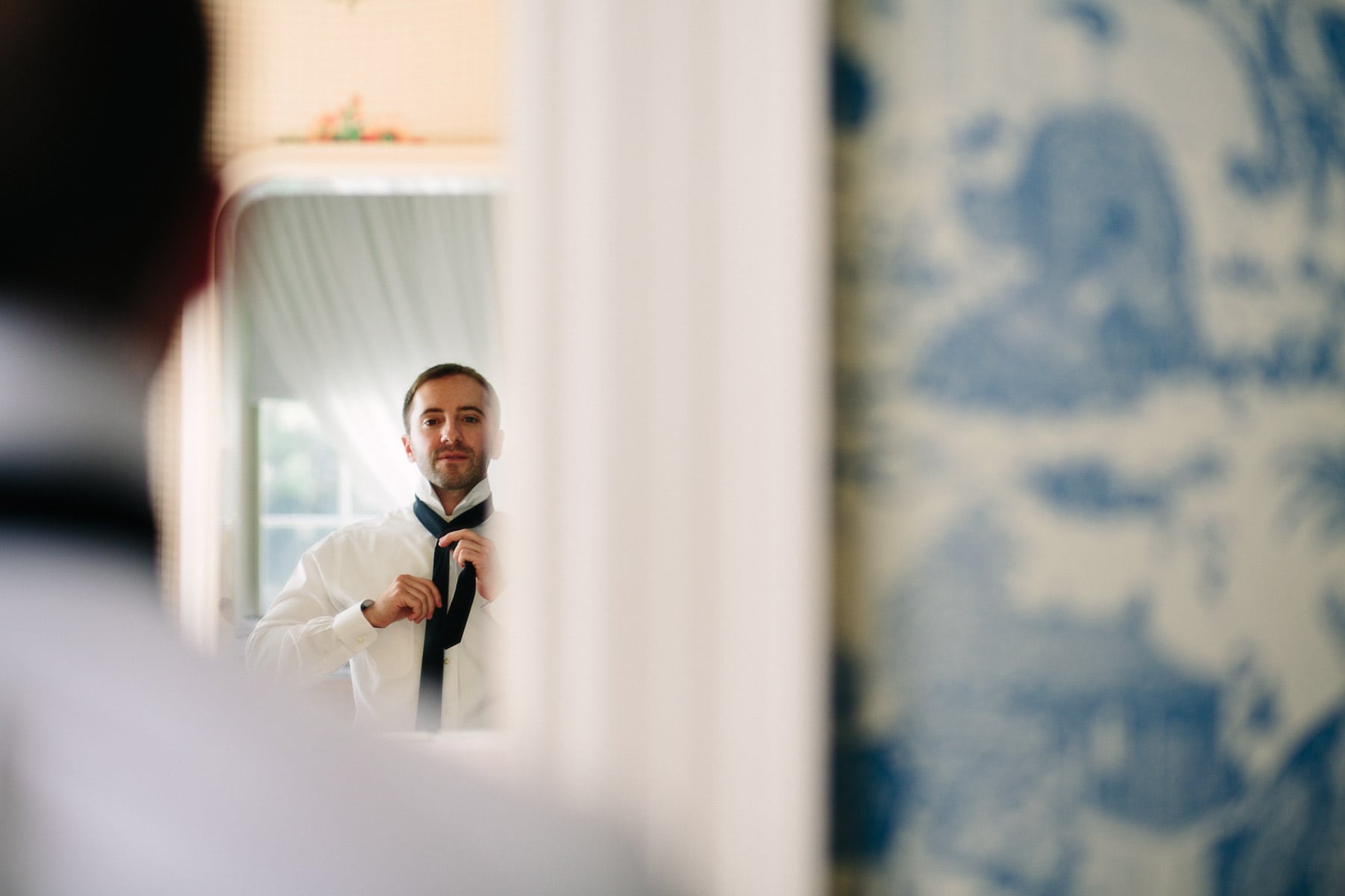 groom tying tie in the blue suite at the Lyman Estate